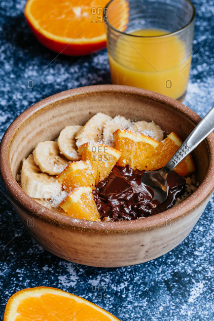 Close up of oatmeal with chia seed, bananas and oranges served in a bowl with a spoon