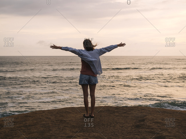 Woman with raised arms standing at the sea at sunset
