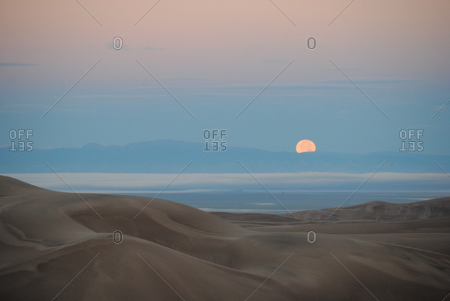 Moon half-setting in sand dunes