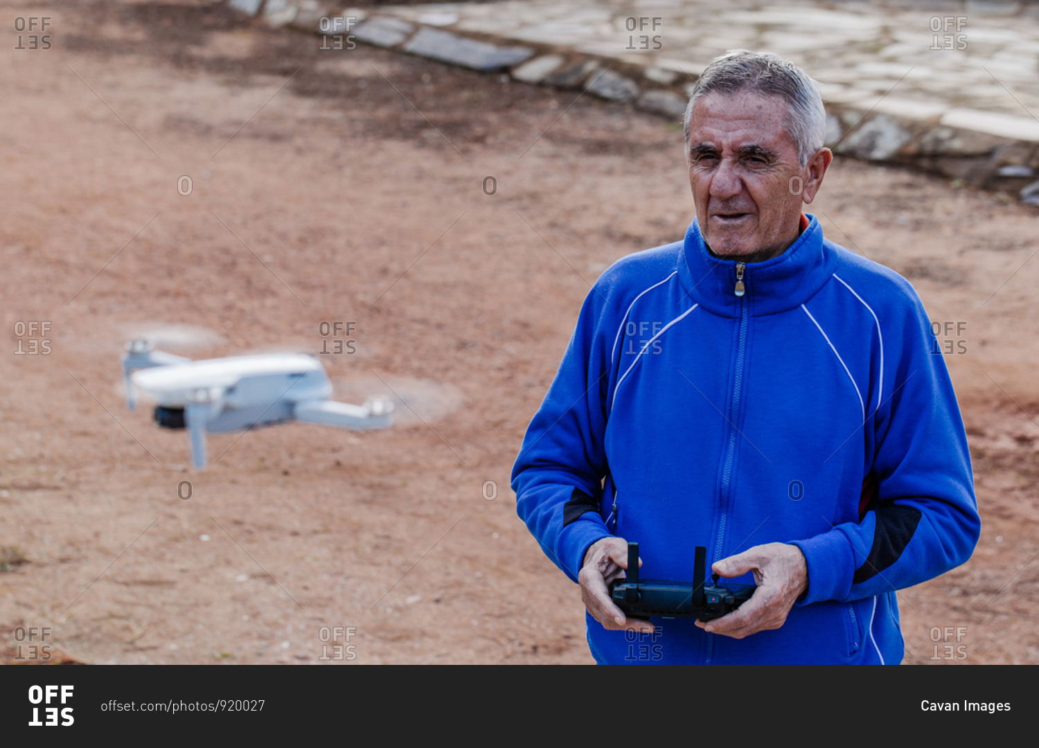 Side view of old man flying the drone looking at the drone while standing against the trees in the park