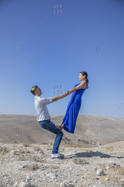 A man is lifting, balancing and supporting a woman in the air in the middle of the desert, allegory for power relations. Acrobalance