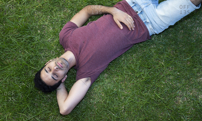 A man or a boy is sleeping or relaxing on the grass, hands behind his head