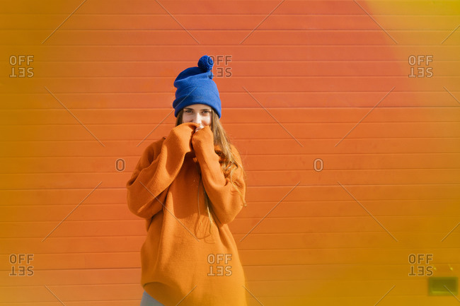 Portrait of teenage girl wearing blue woolly hat and orange sweater in front of orange background