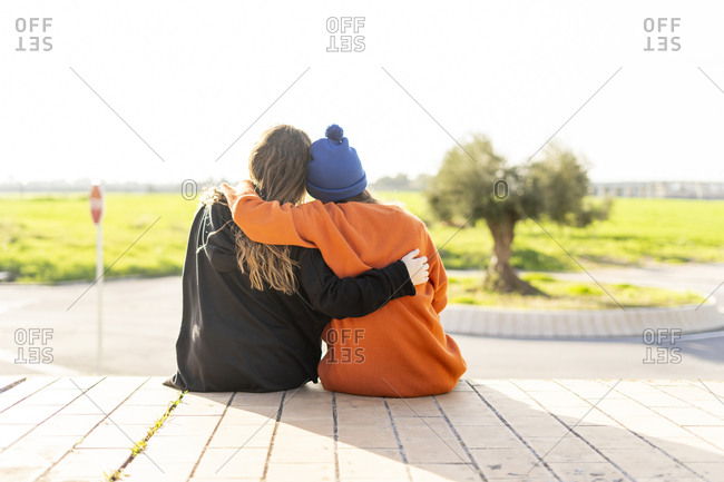 Back view of two teenage girls sitting arm in arm outdoors