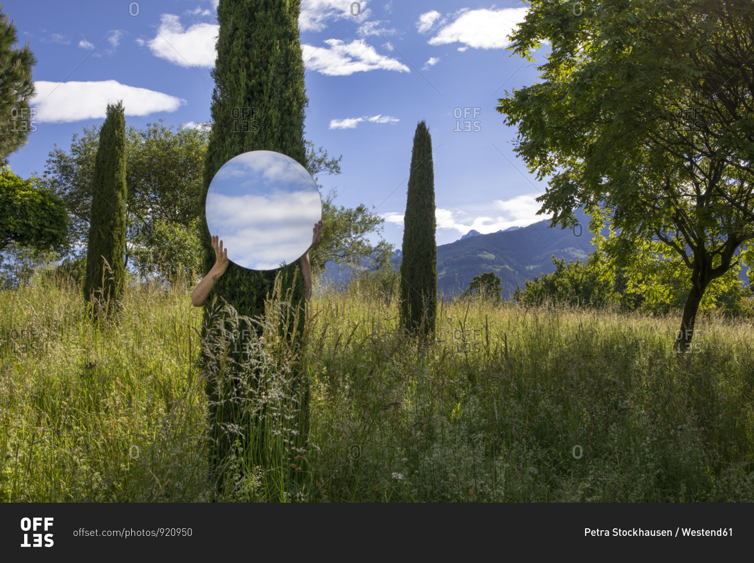 Woman hiding behind tree- holding mirror- reflecting the sky