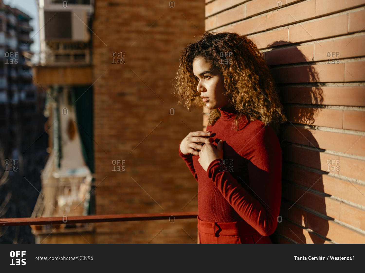 Portrait of young woman wearing red turtleneck pullover and standing on a balcony