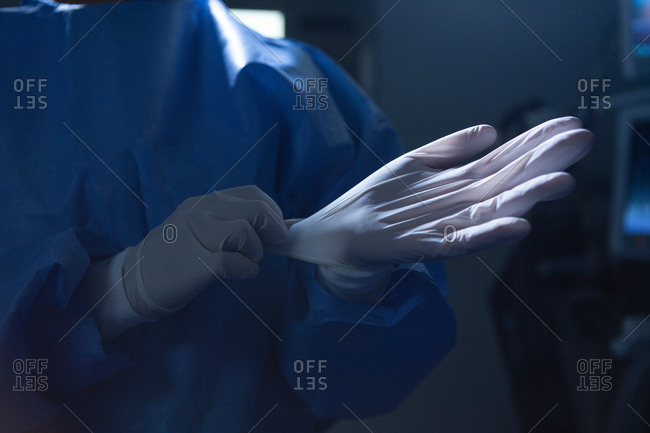 Mid section of mixed-race female surgeon with surgical gloves in operation room in hospital. Shot in real medical hospital with doctors nurses and surgeons in authentic setting