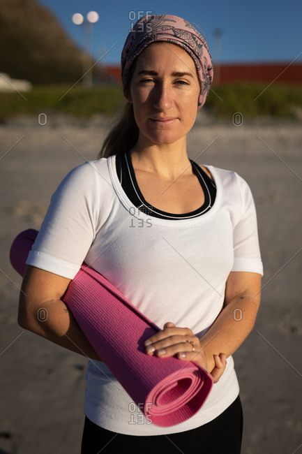 A woman doing yoga on a pink mat on the beach photo – Yoga pants