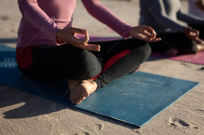 Side view mid section of a multi-ethnic group of female friends enjoying exercising on a beach on a sunny day, practicing yoga sitting in yoga position, meditating in lotus position.