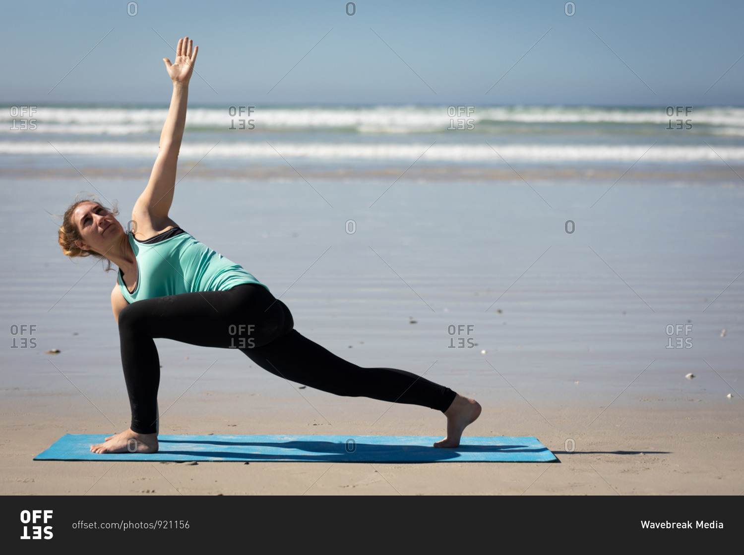 Side view of a Caucasian attractive woman, wearing sports clothes, practicing yoga on yoga mat, stretching in yoga position, on the sunny beach.