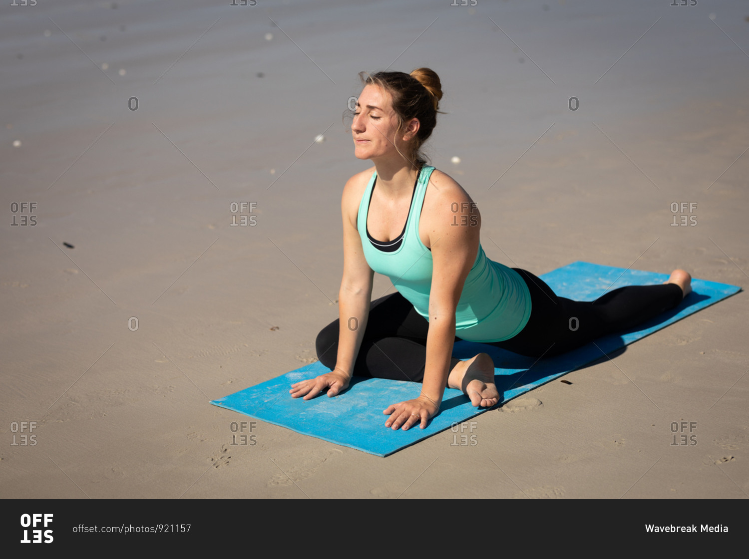 Side view of a Caucasian attractive woman, wearing sports clothes, practicing yoga on yoga mat, stretching in yoga position, on the sunny beach.