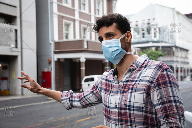 Front view close up of a caucasian man wearing checkered shirt and face mask against air pollution and covid19 coronavirus, hailing a taxi in the street.