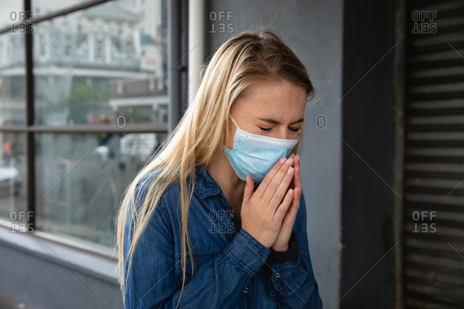 Front view close up of a caucasian woman wearing face mask against air pollution and covid19 coronavirus, walking the street and covering her face while coughing.