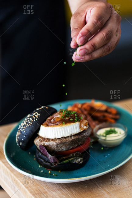 Chef topping a burger with chives