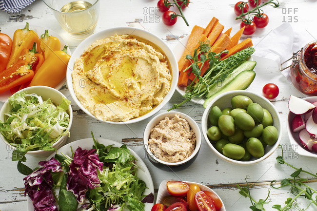 Hummus dip and raw vegetarian snacks on white wooden table.