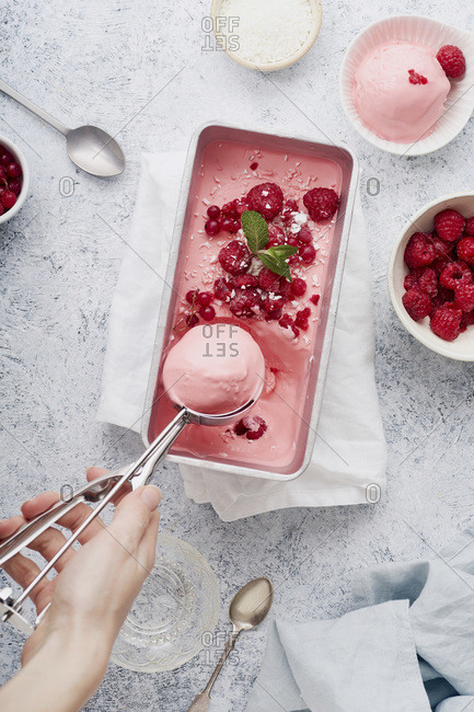 Female hand scooping pink ice cream with raspberries, mint and red currants. Top view
