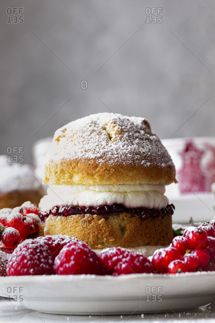 Victoria Sponge Cake with raspberry jam and whipped cream, generously sprinkled with powdered sugar, served with fruits.
