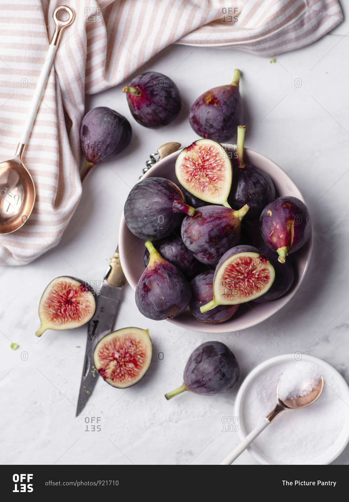 A Bowl Of Ripe, Purple Figs On A White Marble Countertop Surrounded By 