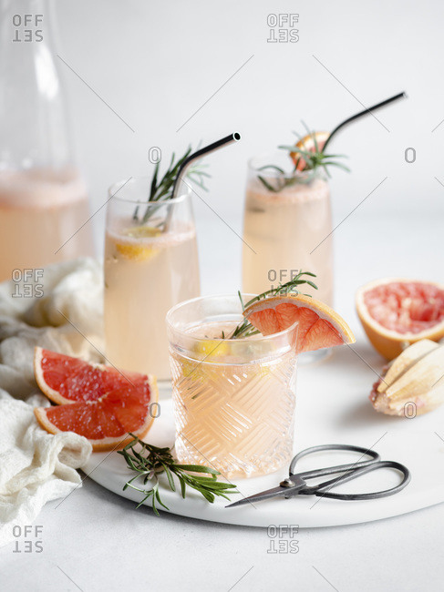 3 glasses of grapefruit cocktail on a marble tray with rosemary and grapefruit slices