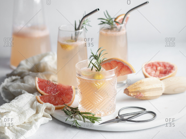 3 glasses of grapefruit cocktail on a marble tray with rosemary and grapefruit slices, pitcher and mousseline napkin
