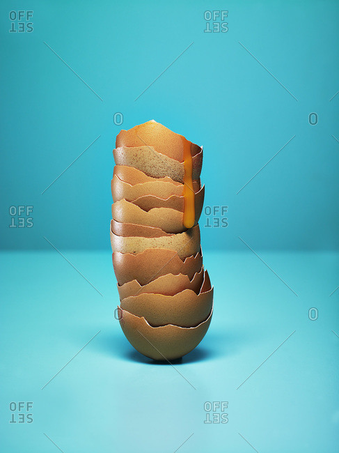 Hen egg shells stacked against a blue background. Yolk dripping down the shells.