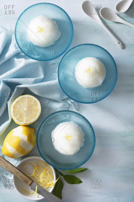 Scoops of lemon sorbet in bowls with twisted strips of lemon zest on top.