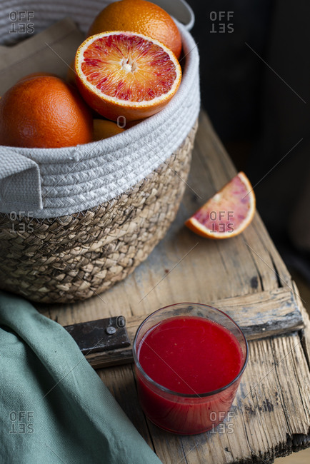 Basket with blood oranges an a wooden table with a glass of red orange juice