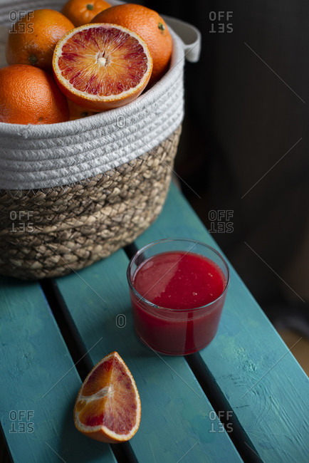 Blood oranges basket on a blue wood table with a glass red orange juice
