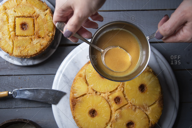 Overhead view of hands pouring Pineapple syrup on an upside down pineapple cake