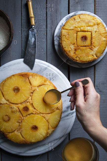 Overhead view of a hand pouring Pineapple syrup on an upside down pineapple cake