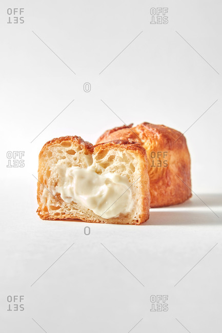 Freshly baked sweet dessert, homemade delicious cut bun with milk cream and another whole bun on a light grey background, soft shadows.