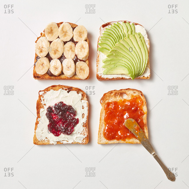 Food pattern from toasts with different topping - fruits and berry jam, avocado vegetable, banana slices and chocolate cream on a light grey background.