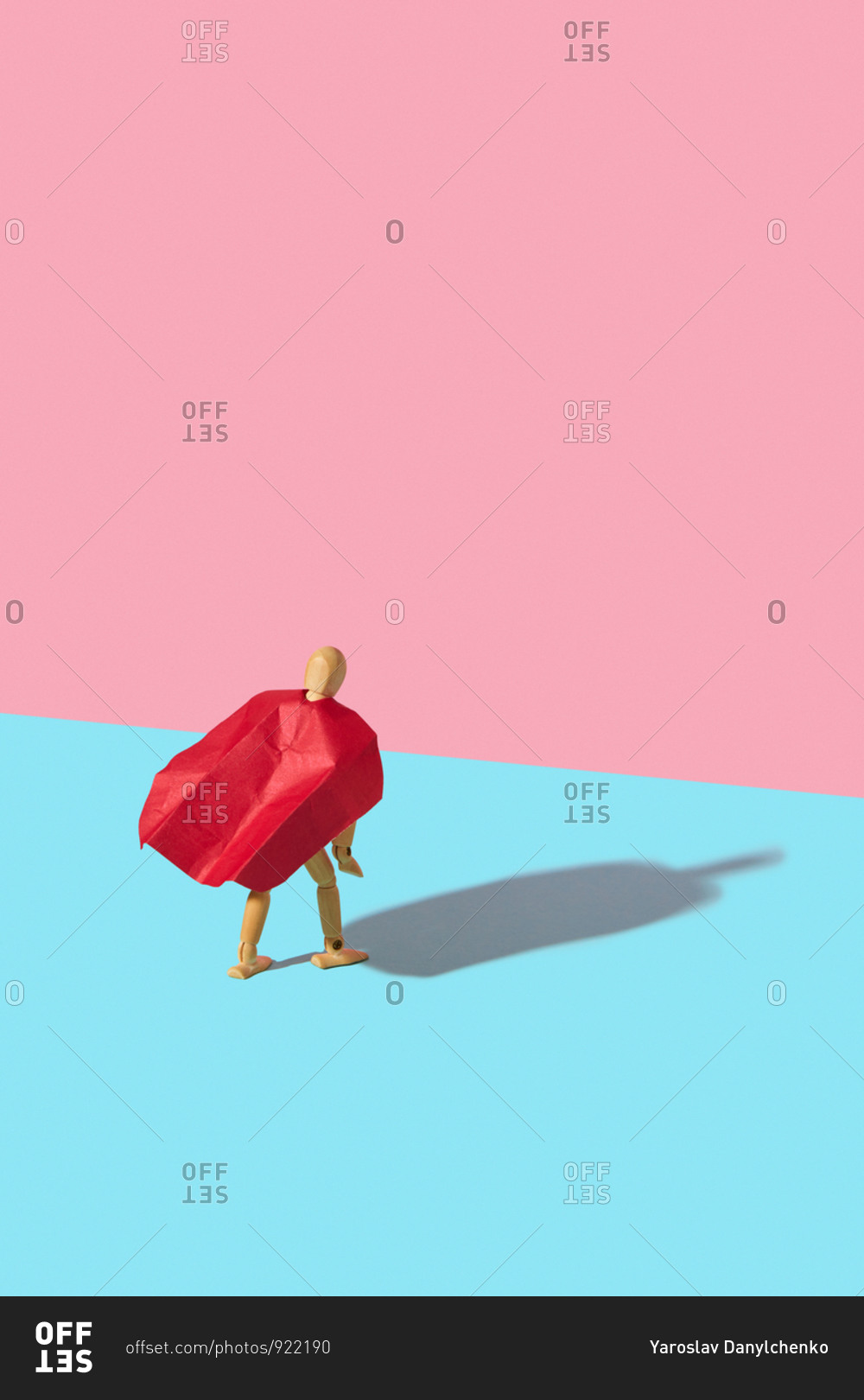 Movable human miniature model in red cape as a superhero or superman is standing on a duotone background with hard shadows.