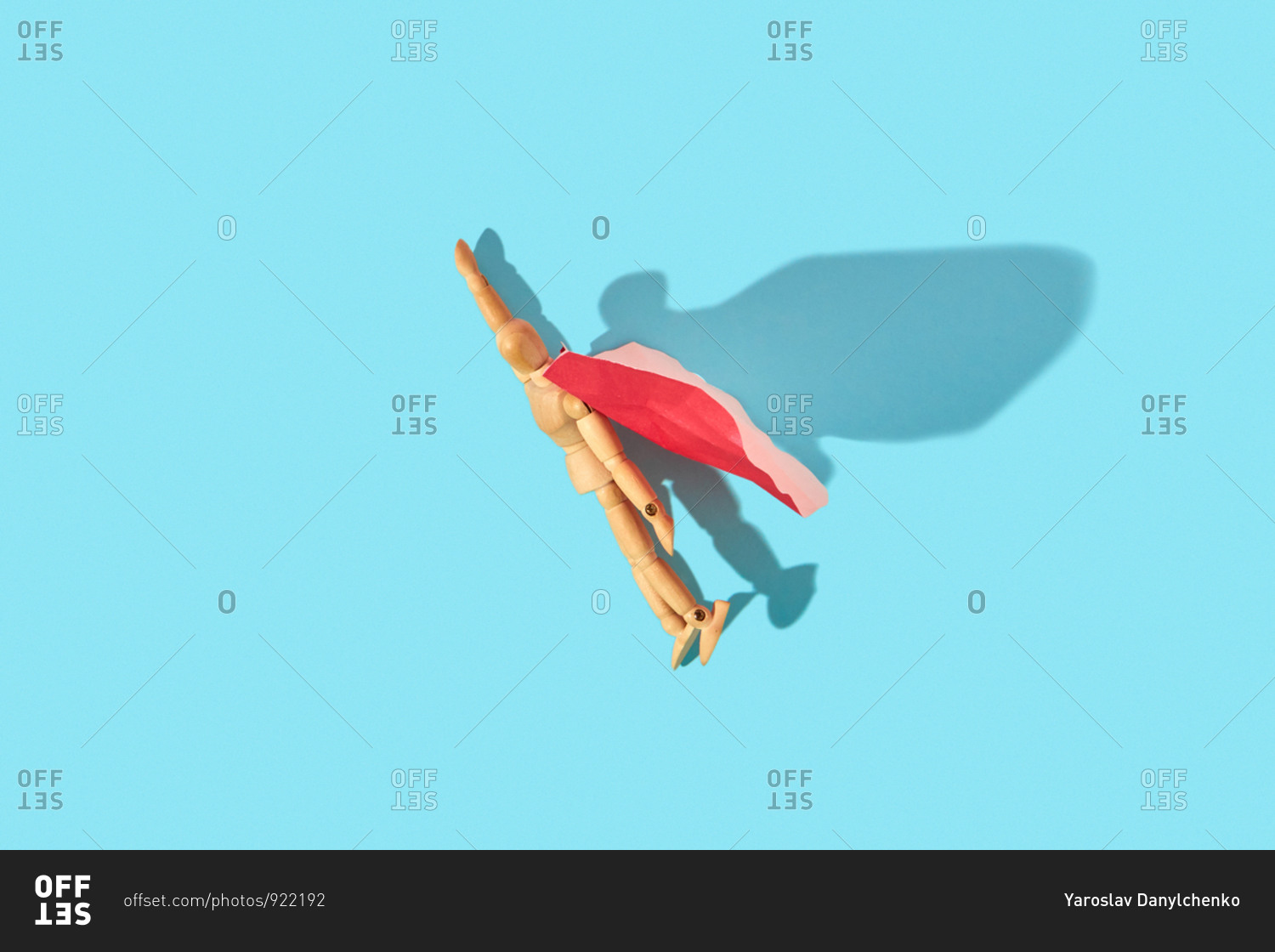 Wooden mannequin miniature doll in a red cape with raised hand flies up as a superman or superhero on a light blue background.