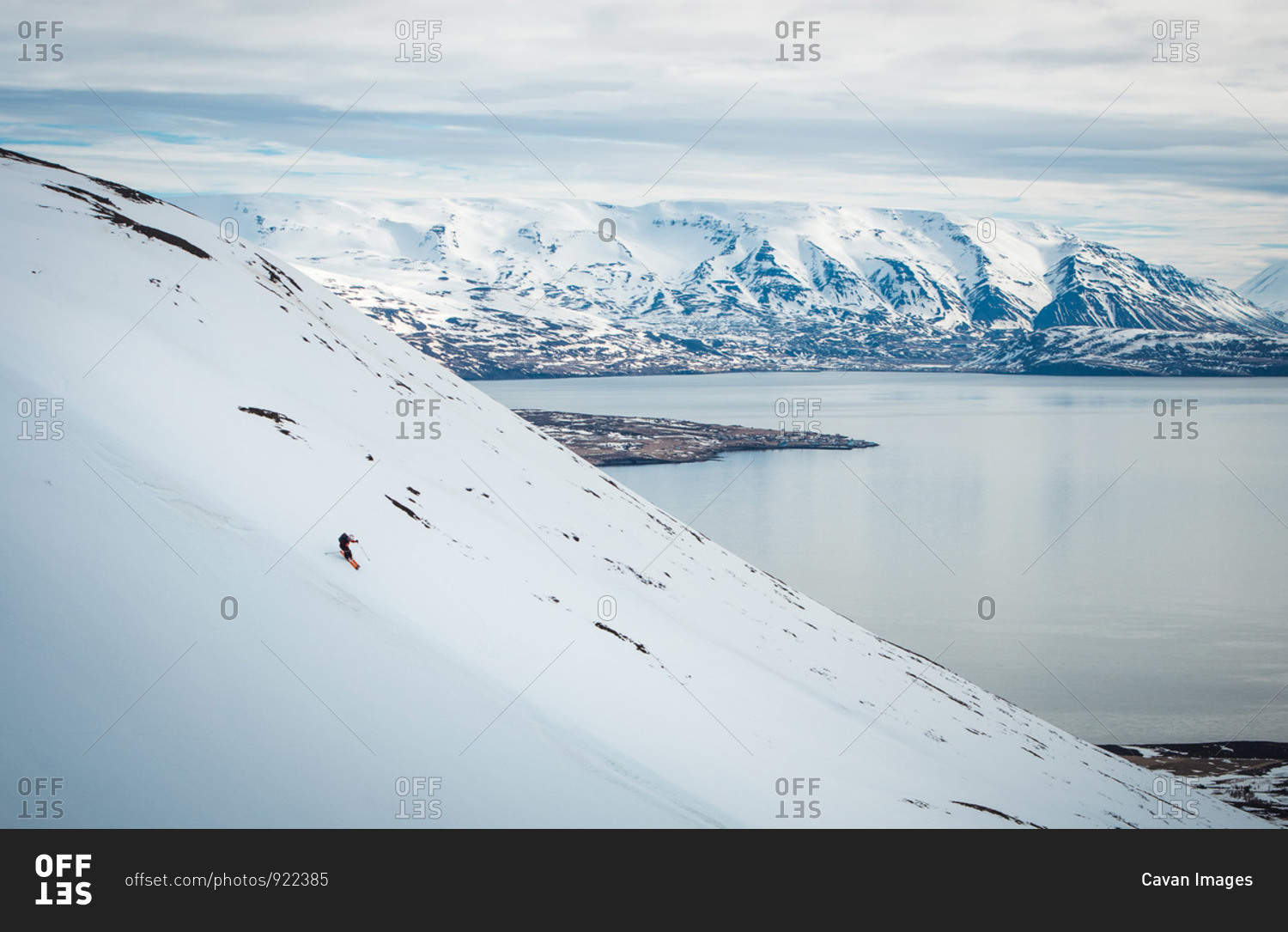 A man skiing down a mountain with snowy mountains and ocean behind