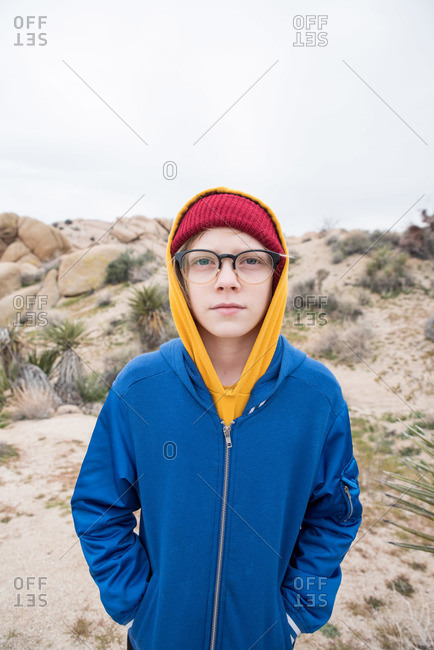 Tween with beanie and glasses in front of small mound in desert