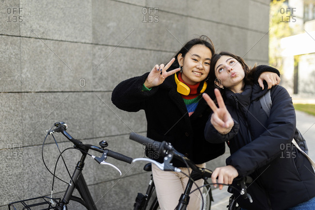 Two best friends showing victory sign while holding bicycles