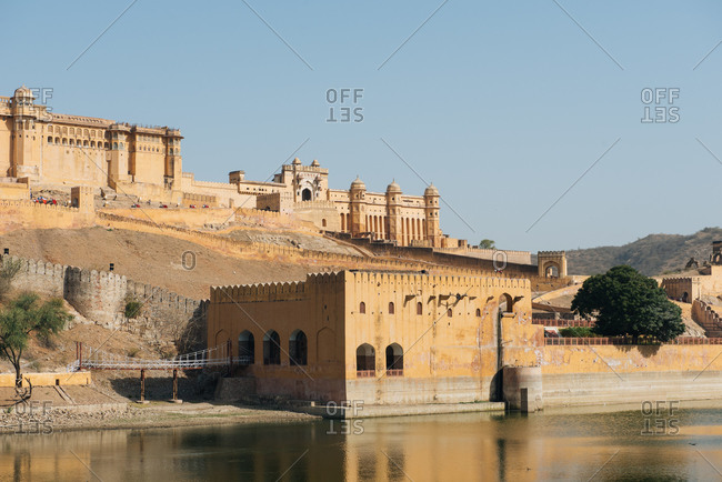 Old stone palace with beautiful architecture located near lake in ancient city of India under clear blue sky