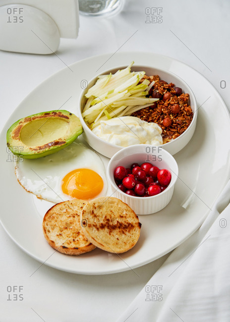 Healthy and balanced breakfast dish with granola, yogurt, apple, cranberries fried egg and grilled avocado