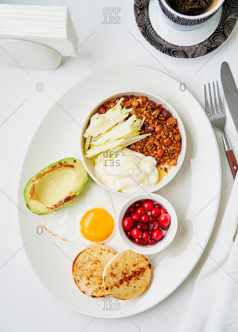 Balanced breakfast dish of homemade granola, yoghurt, sliced apples, sunny side up and grilled avocado