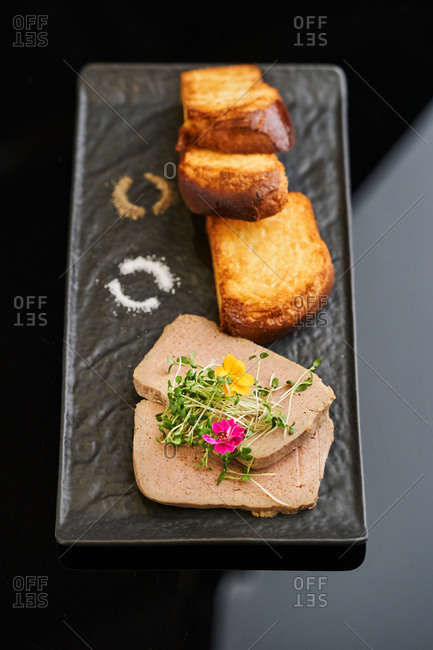 Creamy goose liver pate served with toasted brioche, edible flowers and microgreens on black serving dish