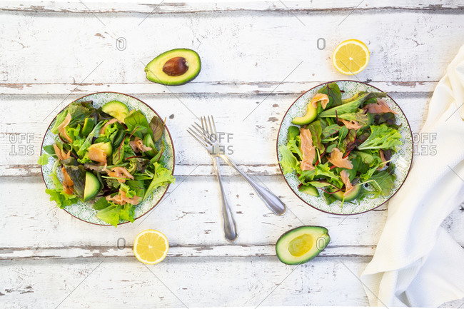 Two plates of ready-to-eat green salad with arugula- Lollo Rosso lettuce- baby spinach- beetroot leaves- avocado- corn salad and salmon