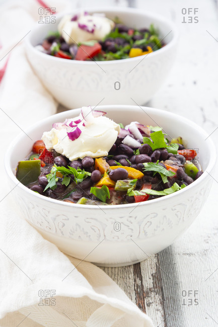 Two bowls of black bean soup with bell pepper- cilantro- sour cream and red onions