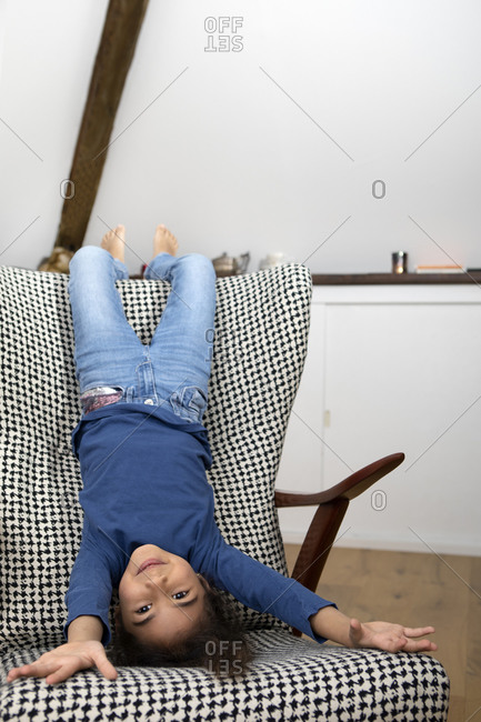 Portrait of little girl hanging upside down from backrest of an armchair