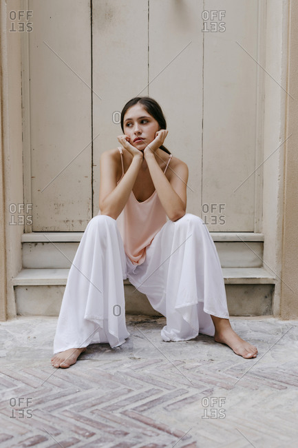 Portrait of melancholic teenage girl wearing white culottes sitting barefoot on steps outdoors