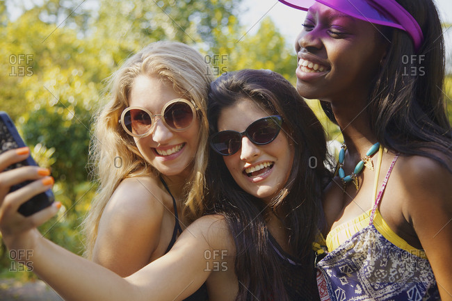 Happy teenage girl friends taking selfie with smart phone on sunny patio