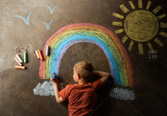 Overhead view of little boy drawing a rainbow with chalk