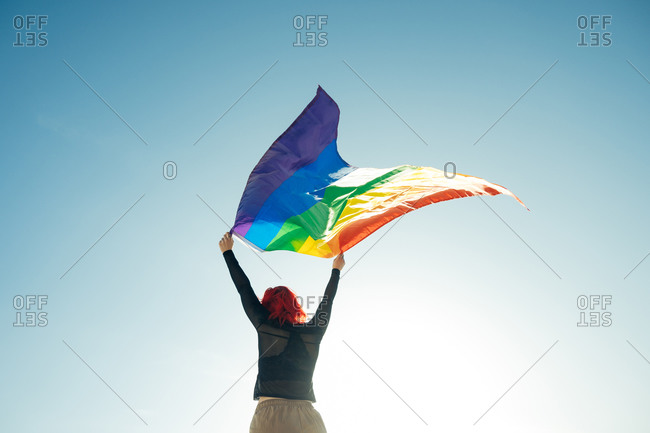 Woman holding the Gay Rainbow Flag on blue sky background. Happiness, freedom and love concept for same sex couples.