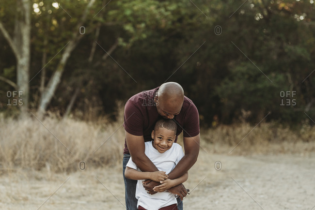 Close up of happy father and son hugging in backlit field