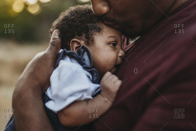 Close up of sweet father kissing newborn girl in backlit field